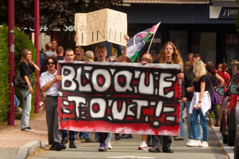 Das Foto zeigt demonstrierende Menschen hinter einem Transparent mit dem Text "Bloque Tout!" (Blockiert Alles!)