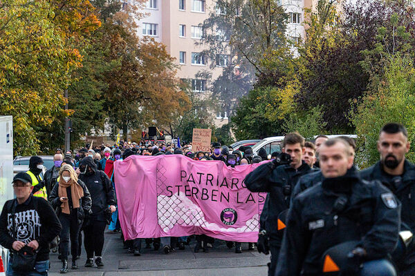 Das Foto zeigt das zur Hälfte von Polizisten verdeckte pinke Fronttransparent "Patriarchat sterben lassen". Dahinter die Demonstration
