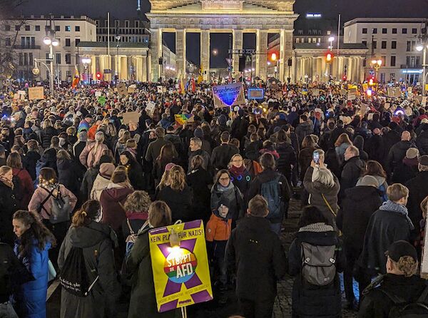 Das Foto zeigt eine große Menschenmenge am Brandenburger Tor mit Lichtern, Transparenten und Texttafeln gegen die AfD und den Rechtsruck