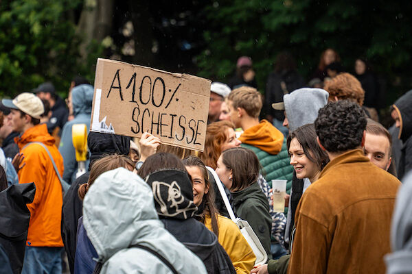 Das Foto von Björn Obmann zeigt einen Auschnitt aus der Demo mit einem Pappschiclt das hoch gehalten wird. Der Text: "A100% SCHEISSE"
