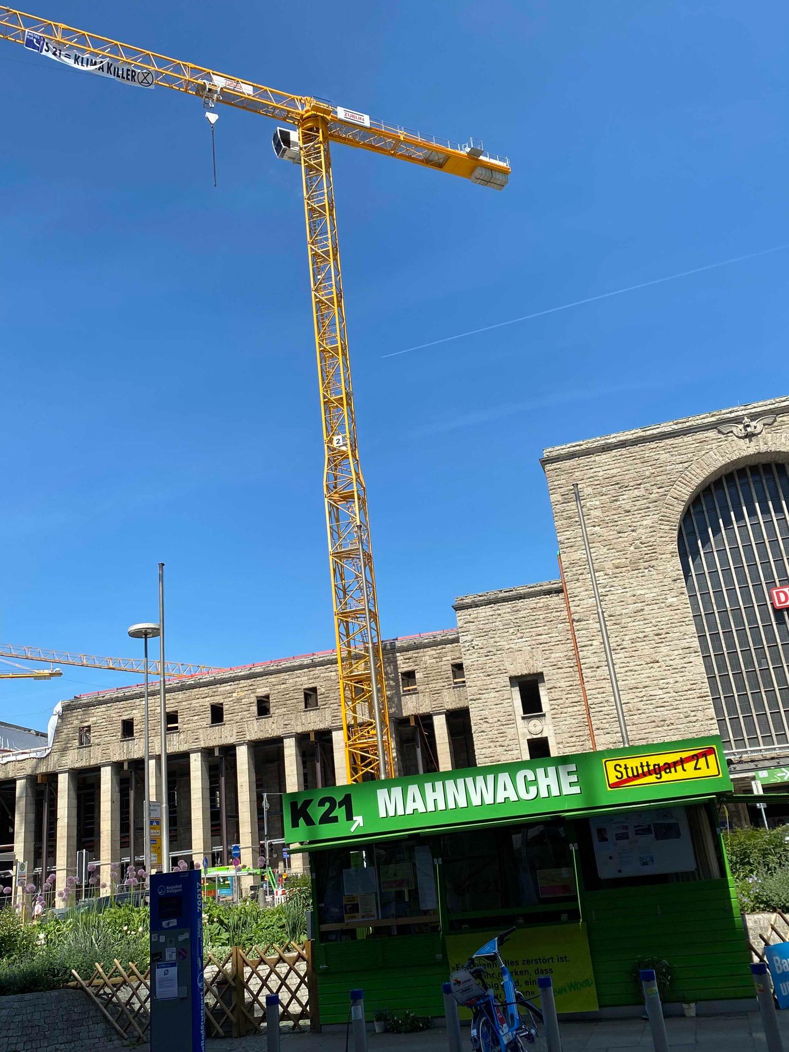 Ausleger des Züblin Kranes, an dem ein Transparent mit der Aufschrift: "S21=Klimakiller", umrahmt von den Logos von "Extinction Rebellion (XR)" und "UMSTIEG21 Plus" hängt. Im Hintergrund das Bahnhofsgebäude, im Vordergrund die Dauermahnwache gegen Stuttgart 21 Quelle: Pressemitteilung der angeklagten Klimaaktivist*innen vom 23.08.2022 Ausleger des Züblin Kranes, an dem ein Transparent mit der Aufschrift: "S21=Klimakiller", umrahmt von den Logos von "Extinction Rebellion (XR)" und "UMSTIEG21 Plus" hängt. Im Hintergrund das Bahnhofsgebäude, im Vordergrund die Dauermahnwache gegen Stuttgart 21 Quelle: Pressemitteilung der angeklagten Klimaaktivist*innen vom 23.08.2022