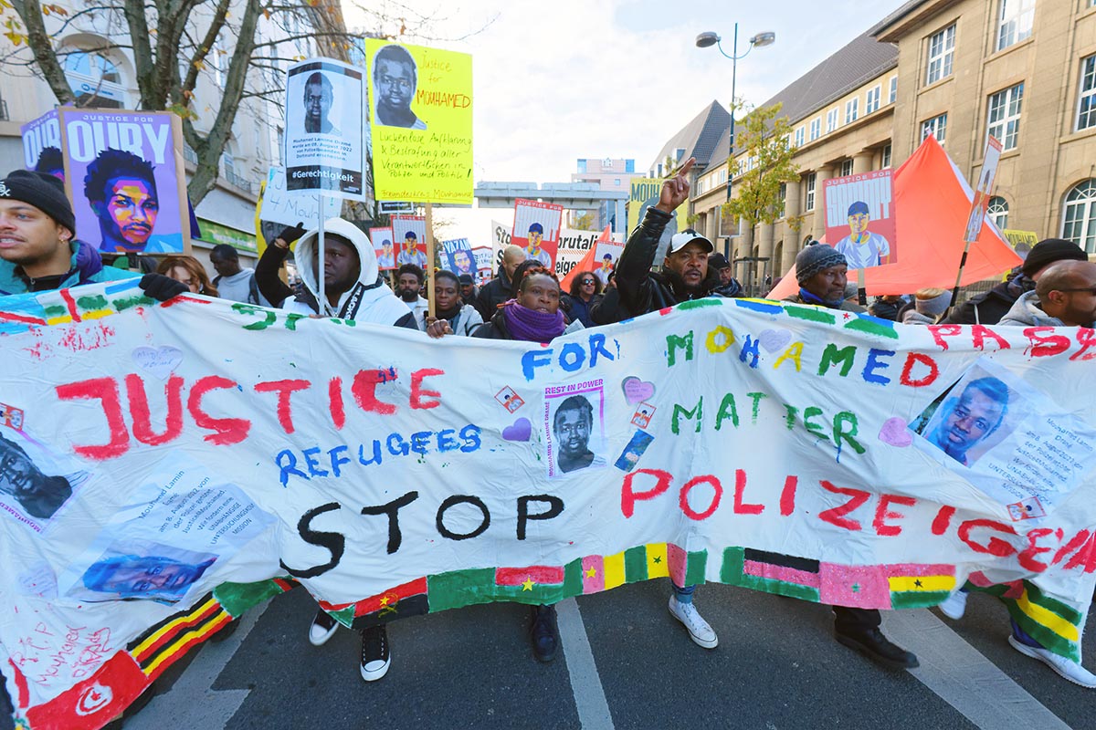 Transparent, getragen von mehreren People of Colour, auf dem steht: 'Justice for Mohamed - Refugees matter - Stop Polizeigewalt' Foto: © Uwe Bitzel via Umbruch Bildarchiv Transparent, getragen von mehreren People of Colour, auf dem steht: 'Justice for Mohamed - Refugees matter - Stop Polizeigewalt' Foto: © Uwe Bitzel via Umbruch Bildarchiv