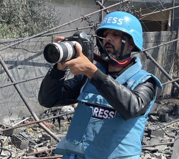 Der preisgekrönte internationale und arabische Fotojournalist Mohammed Al-Zanoun aus Gaza bei der Arbeit mit blauer Pressejacke, Helm und Kamera beim Fotografieren in einem Trümmerfeld