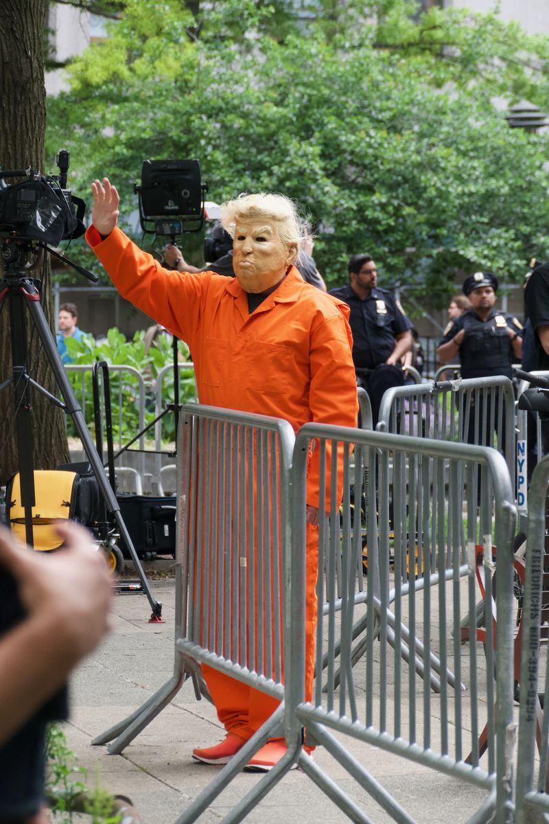 Ein Mann winkt den Medien zu. Er trägt einen orangefarbenen Overall und eine Michael-Meyers-Maske von Trump.