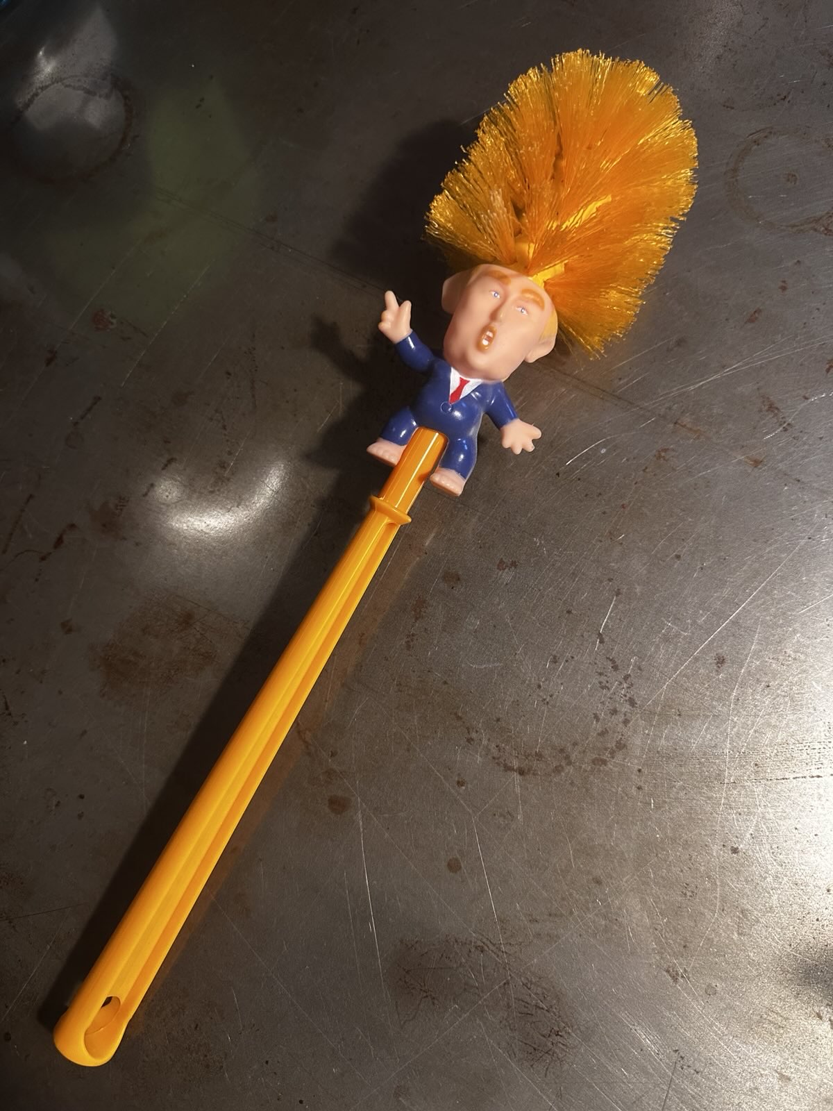 Eine Toilettenbürste, bestehend aus einer Trump Figur und orangefarbenen Borsten