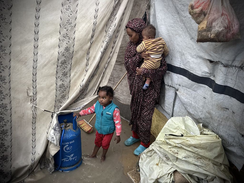 Palästinenser stehen in ihrem überfluteten Familienzelt in einem Vertriebenenlager in Khan Yunis, Gaza-Streifen, 31. Dezember 2024. (Doaa Albaz/Activestills)