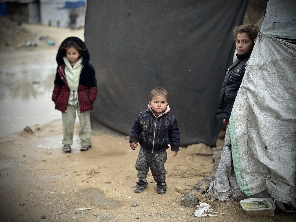 Palästinensische Kinder stehen im Schlamm vor ihrem Familienzelt in einem Vertriebenenlager in Khan Younis, Gaza-Streifen, 31. Dezember 2024. (Doaa Albaz/Activestills)