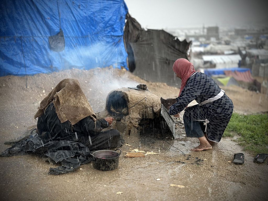Palästinenser kochen unter dem Regen in einem Lehmofen in einem Vertriebenenlager in Khan Yunis, Gaza-Streifen, 31. Dezember 2024. (Doaa Albaz/Activestills)