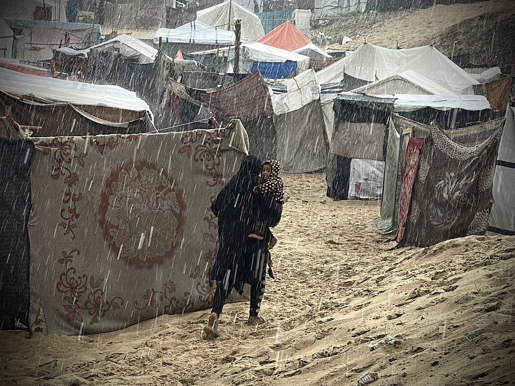 Eine Palästinenserin läuft mit ihrem Kind im Regen durch ein Flüchtlingslager in Khan Yunis, Gaza-Streifen, 31. Dezember 2024. (Doaa Albaz/Activestills)